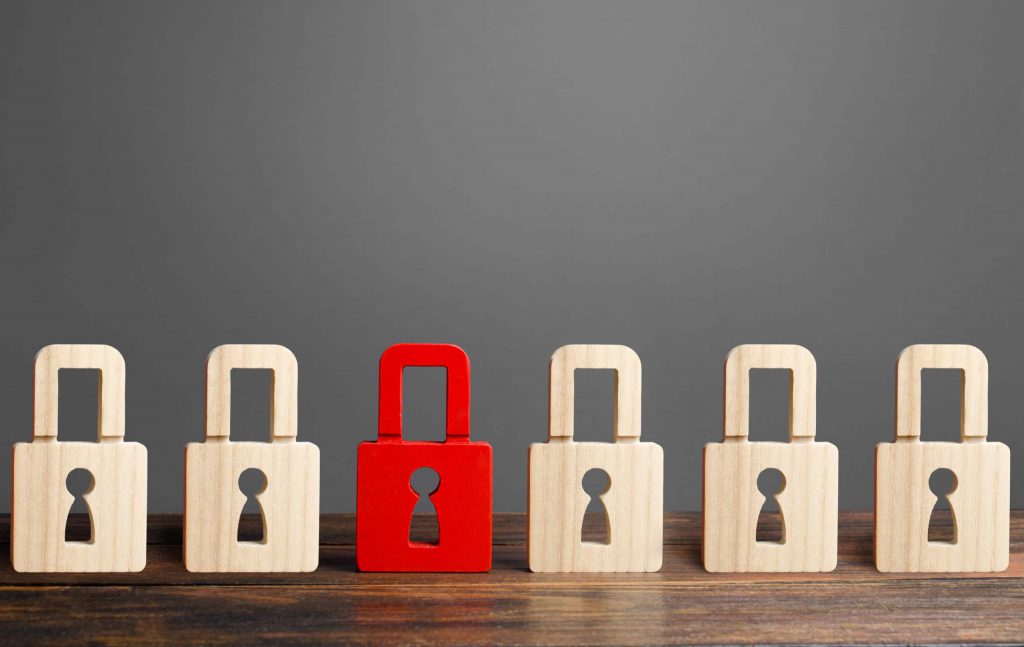 Red wooden padlock with five plain wood padlocks on a wooden table with a grey background.