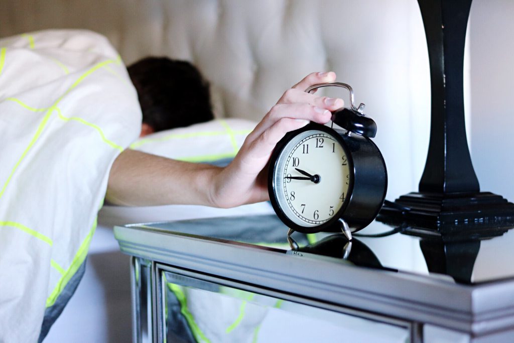 Man lying in bed with hand on an alarm clock.